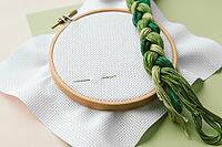 Embroidery tools wooden hoop, green embroidery floss, and needles on white fabric, arranged for needlework and crafting, cross stitch concept [IBR123638384]