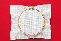 Embroidery hoop with white canvas and two needles placed on vibrant red background, minimalist flat lay symbolizing creativity, traditional craft and artistic inspiration, cross stitch [IBR123638390]