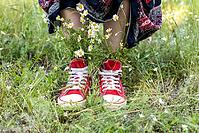 Upturned skirt and naked legs in red shoes with a bouquet of white camomiles in green grass. Summer concept [IBR123639490]