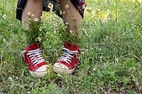 Upturned skirt and naked legs in red shoes with a bouquet of white camomiles in green grass. Summer concept [IBR123639491]