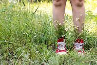 Naked legs in red shoes with a bouquet of white camomiles in green grass. Summer concept [IBR123639492]