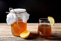 Raw fermented homemade alcoholic or non alcogolic kombucha superfood. Ice tea with healthy natural probiotic in glass with lemon slice on wooden background [IBR123639494]