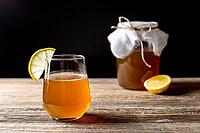 Raw fermented homemade alcoholic or non alcogolic kombucha superfood. Ice tea with healthy natural probiotic in glass with lemon slice on wooden background [IBR123639495]