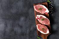 A pieces of raw fresh pork with rosemary on a cutting board on dark background. Meat with spices for recipes and cooking. Top view with copy space [IBR123639505]