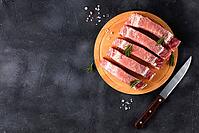 A pieces of raw fresh pork with rosemary on a cutting board on dark background. Meat with spices and knife for recipes and cooking. Top view with copy space [IBR123639506]