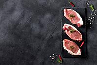 A pieces of raw fresh pork with rosemary on a cutting board on dark background. Meat with spices for recipes and cooking. Top view with copy space [IBR123639507]