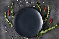 Empty black plate with rosemary branches and spices on a dark background. Top view with copy space [IBR123639523]