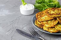 Fritters from zucchini in grey plate with sour cream sauce and greens. Vegetable pancakes of courgettes with green salad on grey background. with copy space [IBR123639574]