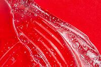 Transparent skincare product on red. Cosmetic gel smudge with bubble. Liquid lotion splash. Serum gel. Hyaluronic acid smear. Lubricant sample. Moisturiser with vitamin. Sexy jelly texture [IBR123646496]