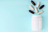 White medical pills and capsules spilling out of bottle. Medication in white container on blue background. Healthcare, health insurance, medicine concept. Copy space, front view [IBR123646511]