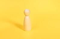 One wooden female figurine stands alone on yellow backdrop isolated. Confident independent person, mentor, coach, leader concept. Front view [IBR123646519]