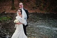 Lovely newlyweds background waterfall at cold autumn day [IBR123675131]
