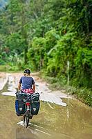 Female cyclist cycling on Trans-sumatran Highway in Sumatra, Indonesia [IBR123713395]