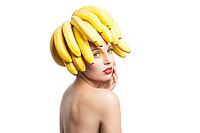 Beautiful fragile model with bunch of bananas on head looking away.Studio shot [IBR123723188]
