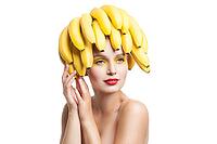 Beautiful fragile model with bunch of bananas on head looking away.Studio shot [IBR123723189]