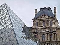 Paris, France - December 10, 2025: The ornate Renaissance facade and the iconic glass Pyramid of the Louvre Museum with multiple tourists scattered across the vast cobblestone courtyard [IBR123895591]