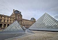 Paris, France - December 10, 2025: The ornate Renaissance facade and the iconic glass Pyramid of the Louvre Museum with multiple tourists scattered across the vast cobblestone courtyard [IBR123895592]