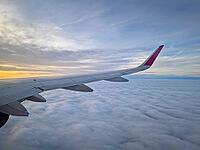 Peaceful aerial view from airplane window to the large wing soaring over a sea of clouds with the sun rising above the horizon, casting a warm glow and illuminating the cloudscape during flight [IBR123895598]