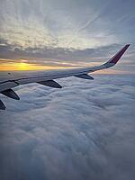 Peaceful aerial view from airplane window to the large wing soaring over a sea of clouds with the sun rising above the horizon, casting a warm glow and illuminating the cloudscape during flight [IBR123895599]