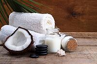 Spa setting and health care items, coconut, body oil, bath salt, milk, massage stones and towels, on wooden board [IBR123999892]