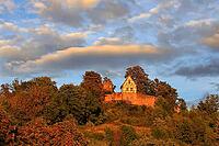 This atmospheric photo captures Königsberg Castle in Bavaria during the golden hour. The eye is drawn to the characteristic building with its red and white half-timbered gable, which was built on a massive stone wall. A square observation tower rises up b [IBR124192776]