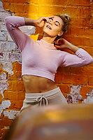 Sexy attraction, a smiling young woman poses playfully against a bright orange brick wall under sunlight, feeling sexy, desires, sexiness, attraction, stretching, stretch, insightful, attractive, wistful, leisure, casual, informal, relaxed, laid-back, ten [IBR124192783]