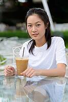 Portrait of young beautiful Asian woman relaxing at the coffee shop with nature outdoors [IBR124309059]