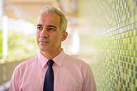 Portrait of handsome Persian businessman with gray hair at the footbridge in the city [IBR124309079]