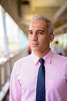 Portrait of handsome Persian businessman with gray hair at the footbridge in the city [IBR124309083]