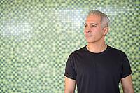 Portrait of handsome Persian man with gray hair against green wall outdoors [IBR124309084]