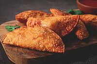 Fried mini chebureks, close-up, on a wooden chopping board, dark background, no people [IBR124476267]