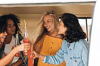 Four women toasting with bottles while sitting in camper van [IBR124491533]