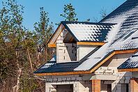 The construction of a home is in progress, with snow lightly dusting the roof and the block walls under a clear blue sky [IBR124491544]