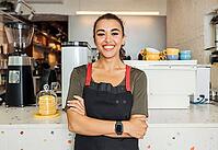 Female barista standing arms crossed in a cafe. Smiling waitress looking at camera while standing in front of a counter [IBR124491549]