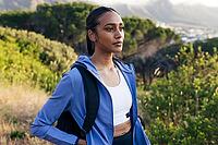 Portrait of young female in sportswear with backpack standing outdoors at sunset [IBR124491568]