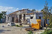 Exterior shot of a house in the process of being built. The structure features exposed cinder blocks and wooden scaffolding under a blue sky [IBR124491585]