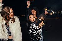 Group of multi ethnic girls with sparklers walking on street at night [IBR124491591]