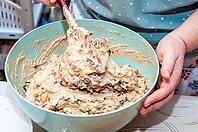 A person is mixing cake batter in a bowl with a spatula, preparing for baking. Various ingredients are visible within the mixture, ready to be baked [IBR124491603]
