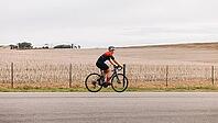 Woman cyclist exercising outdoors on road bike against agriculture field [IBR124491616]