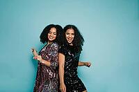 Female friends dancing back to back in studio against blue background [IBR124491627]