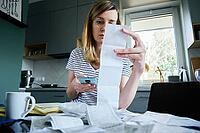 Woman looking at paper bill and counting expenses, Planning budget and home finance management [IBR124497430]