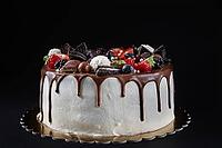 Birthday cake on dark background with copy space. Close up of cake decorated with fresh berries and chocolate sweets on dark background. Delicious dessert for party [IBR124497433]