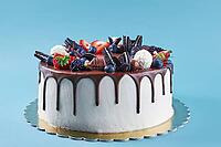 Birthday cake on blue background. Close up of cake decorated with fresh berries and chocolate sweets on color background. Delicious dessert for party [IBR124497458]