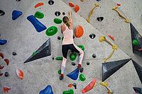 Woman climbing up on wall at bouldering gym. Female climber training, hanging on bouldering climbing wall. Active lifestyle and extreme sport concept [IBR124497464]