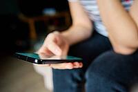 Woman using mobile phone at home. Female sitting on sofa and browsing social networks on smartphone [IBR124497508]