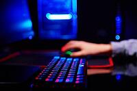 Teenager boy play computer video game in dark room, use neon colored rgb mechanical keyboard, workplace for cybersport gaming [IBR124497509]
