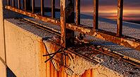Rusty metal fence over cracked concrete at sunset, highlighting decay and texture, construction materials failure concept, AI generated [IBR124550808]