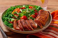 Delicious grilled duck breast served with fresh garden salad and cherry tomatoes at a rustic dining table [IBR124552172]