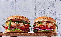 Two shrimp burgers and buns with sesame seeds, bacon, lettuce, tomatoes and onions, On a wooden board [IBR124552185]