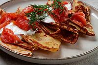 Delicious pancakes with salmon and sour cream, breakfast, on a plate, rustic style, with cutlery [IBR124552186]